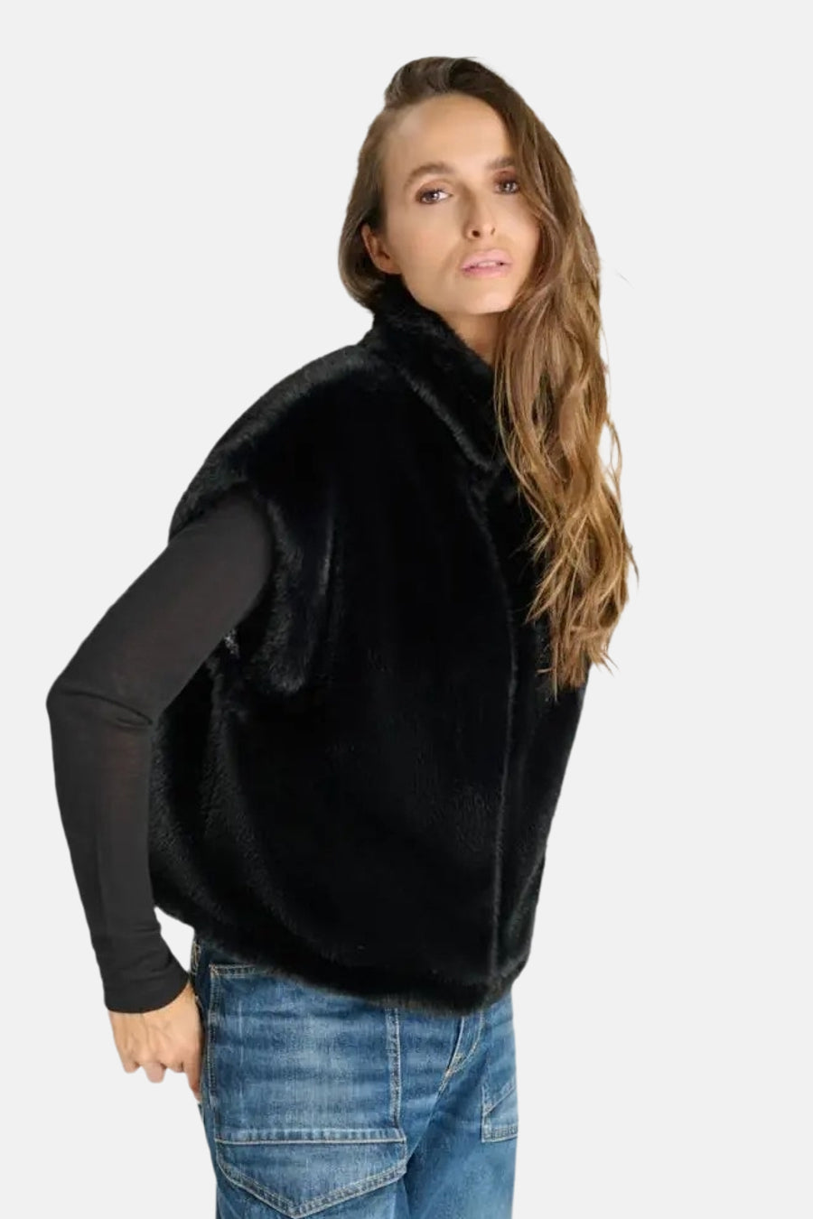 Veste sans manches noire en fausse fourrure douce, par Le Temps des Cerises, portée avec un haut noir et jeans délavés, vue de profil.