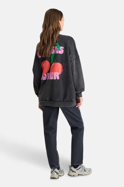 Grijze rondehals sweatshirt van Le Temps des Cerises met kersenprint op de rug, gedragen met een zwarte jeans en sneakers.
