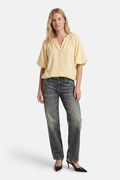 Yellow 3/4 sleeve blouse with gathered neckline and flowy sleeves, worn with distressed jeans and black heels, full-length front view