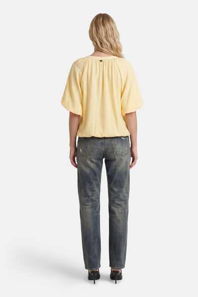 Yellow 3/4 sleeve blouse with gathered back neckline, shown from rear on model wearing distressed jeans and black heels.