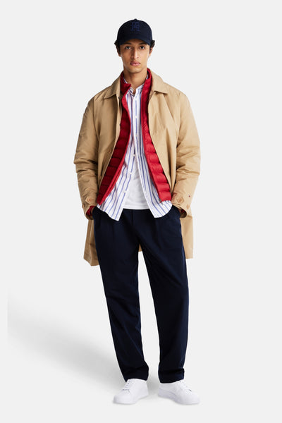 Witte Tommy Jeans sneakers, gedragen met een marineblauwe broek, een gestreept overhemd en een beige trenchcoat.