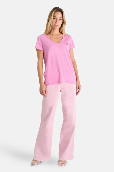 T-shirt rose à manches courtes par Le Temps des Cerises, porté avec un pantalon rose et des sandales blanches.