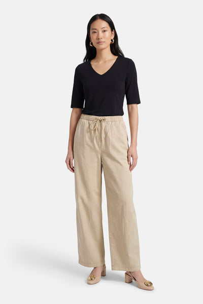 Pantalon beige, ADORE, avec cordon de serrage, porté avec un t-shirt noir et des escarpins beiges à talons.
