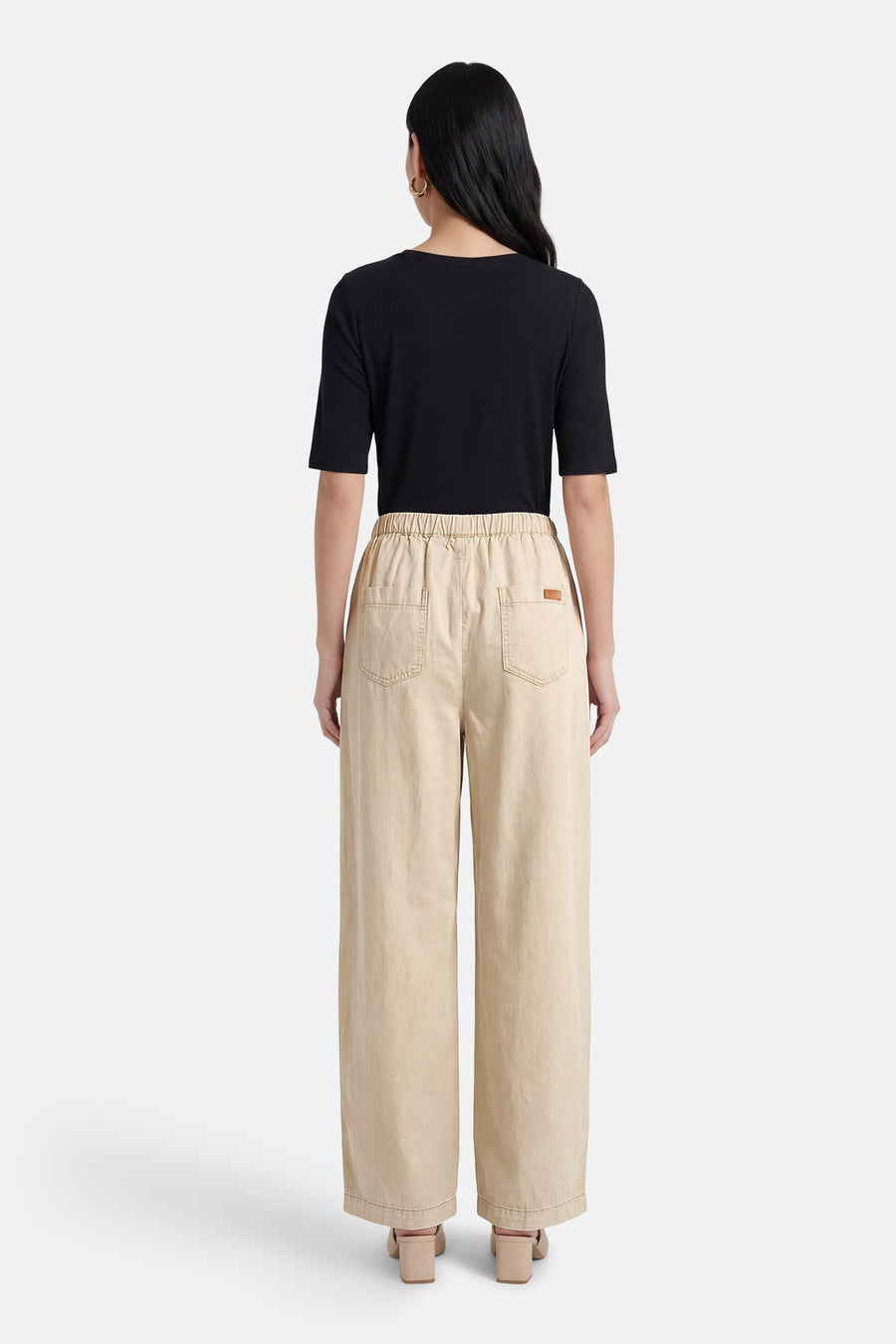 Pantalon beige ADORE, coupe ample avec taille élastiquée et poches arrière, porté avec un t-shirt noir et des chaussures à talons carrés.