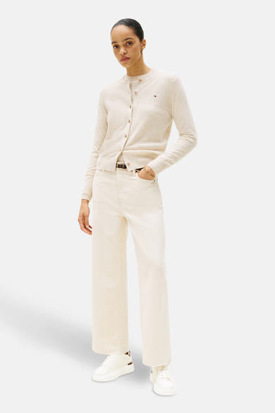 Baskets blanches de TOMMY JEANS, avec une semelle épaisse et lacets, portées avec un jean et un cardigan.
