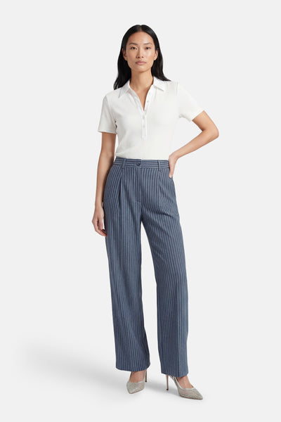 Blauwe kostuumbroek van ADORE, met verticale strepen, gedragen met een witte polo en glinsterende pumps.