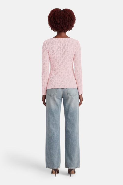 T-shirt rose à manches longues de AMELIE ET AMELIE, avec motif en dentelle délicate, porté avec un jean ample et des talons hauts.