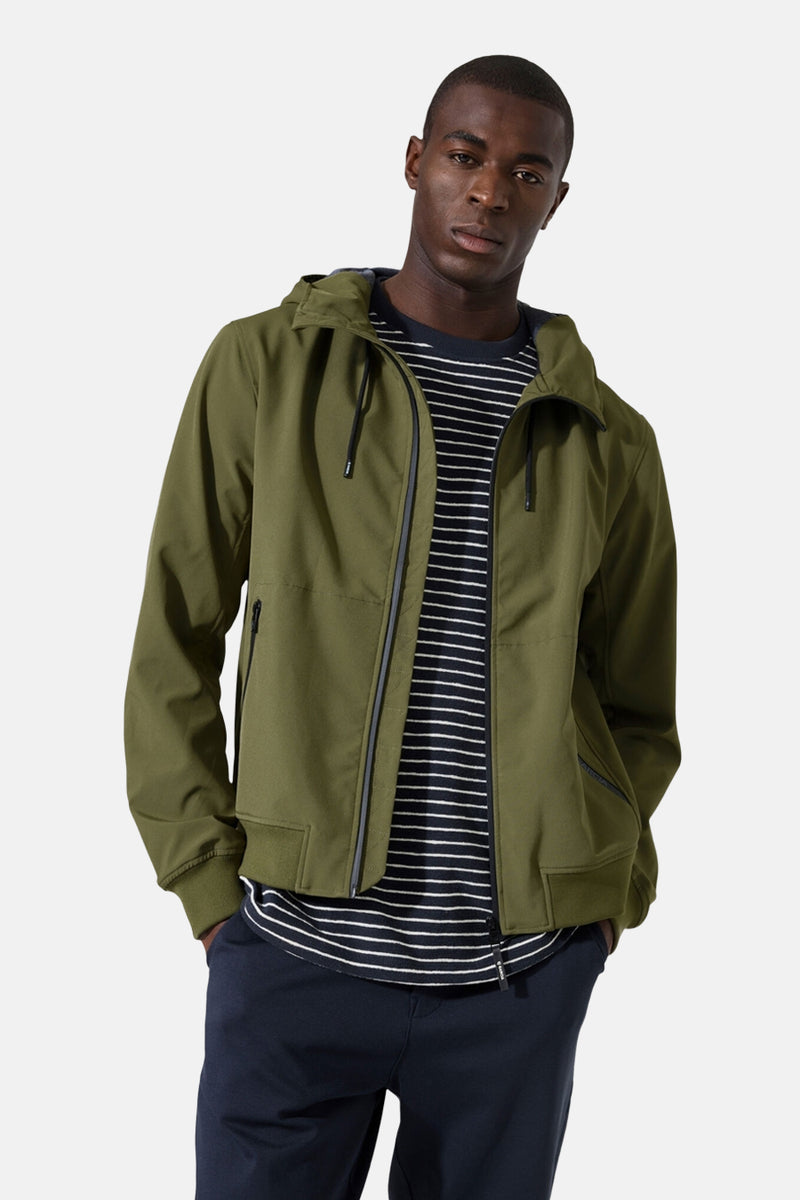 Imperméable olive par GARCIA avec capuche et fermeture éclair, porté sur un t-shirt rayé et un pantalon bleu marine.
