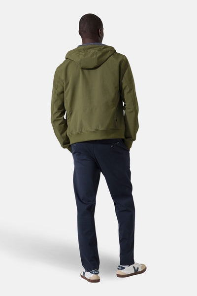 Imperméable olive de GARCIA, avec capuche et détails de style, porté avec un pantalon bleu marine et des baskets.