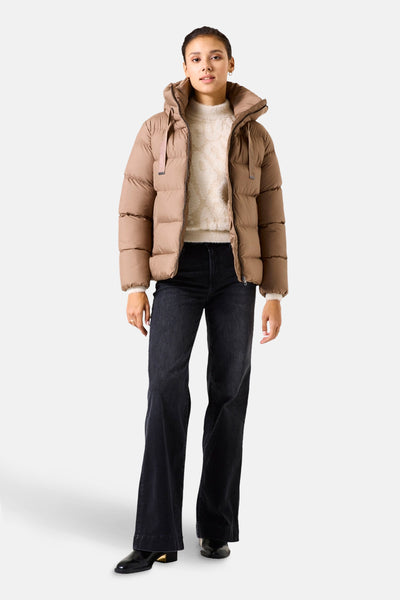 Korte beige jas van GARCIA, gewatteerd met capuchon, gedragen met een wollen trui en een zwarte flared jeans.