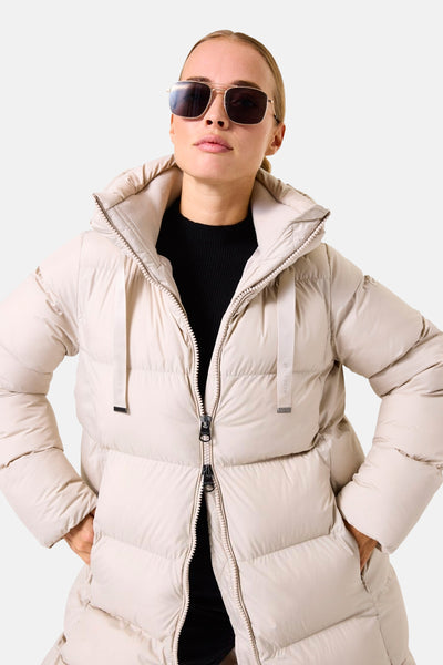 Veste longue écru de GARCIA, avec fermeture éclair et capuche, portée sur un pull noir.
