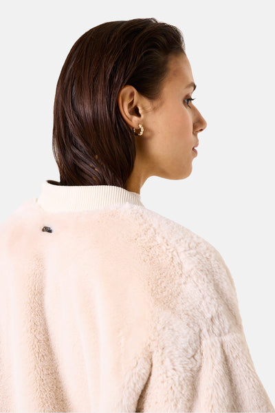 Veste courte beige de GARCIA, en fausse fourrure douce, avec col montant et bijou d'oreille doré visible.