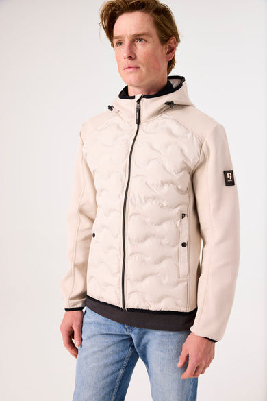 Beige regenjas van GARCIA, met capuchon en ritssluiting, gedragen over een grijs T-shirt en een blauwe spijkerbroek.