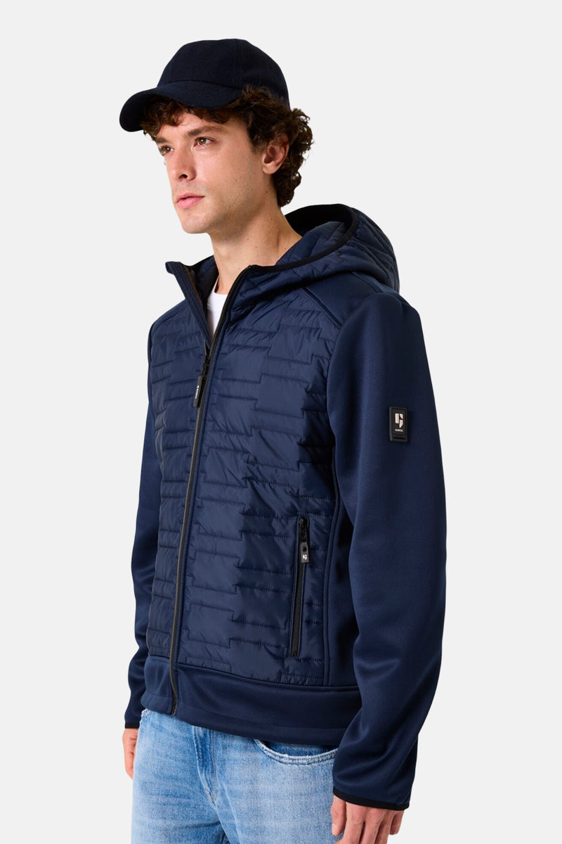 Veste de pluie bleue de GARCIA, avec capuche et fermeture éclair, portée avec un jean et une casquette.
