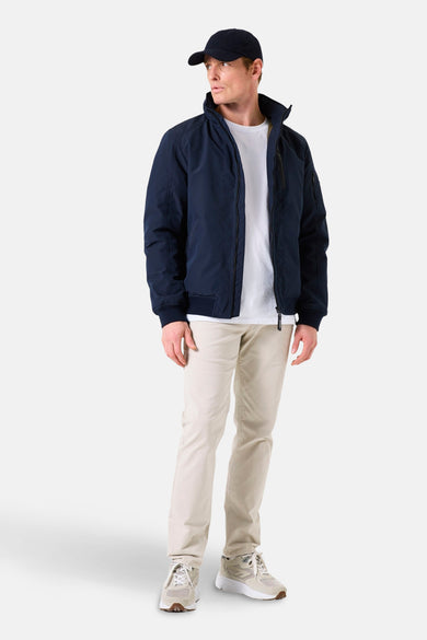 Veste de pluie bleue de GARCIA, portée avec un t-shirt blanc, un pantalon beige et des baskets.