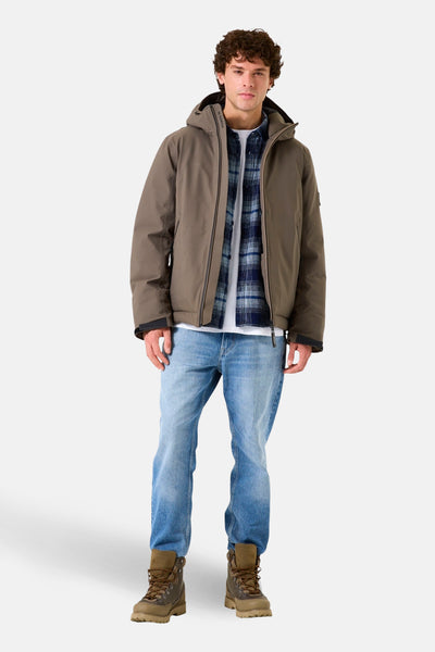 Veste de pluie kaki de GARCIA, portée sur une chemise à carreaux et un t-shirt blanc, avec un jean et des chaussures de randonnée.