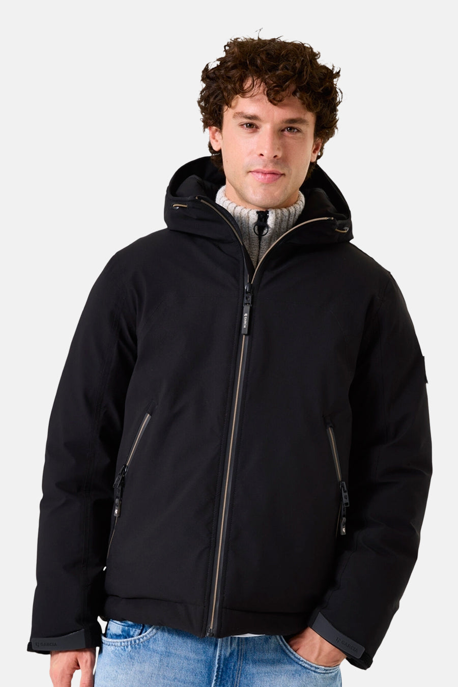 Veste de pluie noire de GARCIA, avec capuche et fermeture éclair, portée sur un pull en maille et un jean clair.