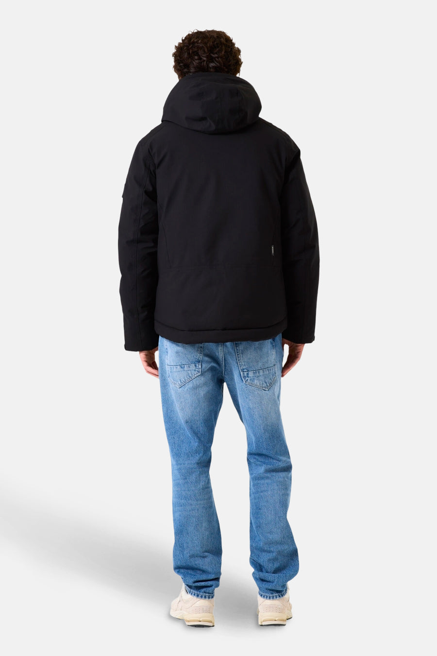 Veste de pluie noire de GARCIA, vue de dos, portée avec un jean bleu et des baskets crème.