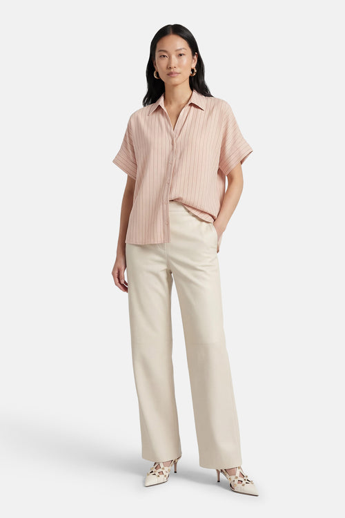 Chemise beige à rayures verticales par AMELIE ET AMELIE, portée avec un pantalon crème et des chaussures à talons blanches.
