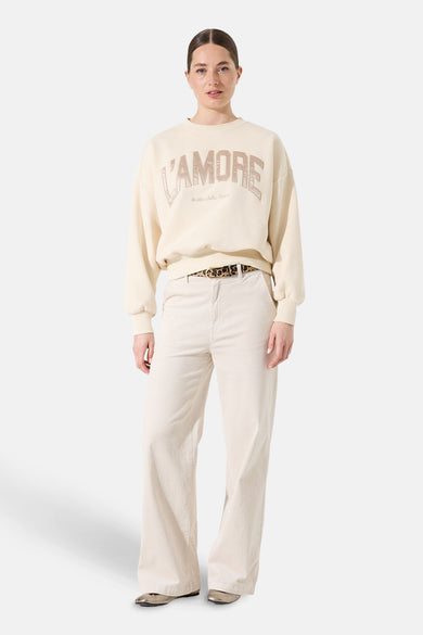 Sweat écru de GARCIA, avec inscription "L'amore", porté avec un pantalon beige à ceinture imprimée léopard.
