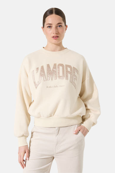 Sweat écru de Garcia avec inscription décorative "L'amore" et pantalon beige en velours côtelé porté.
