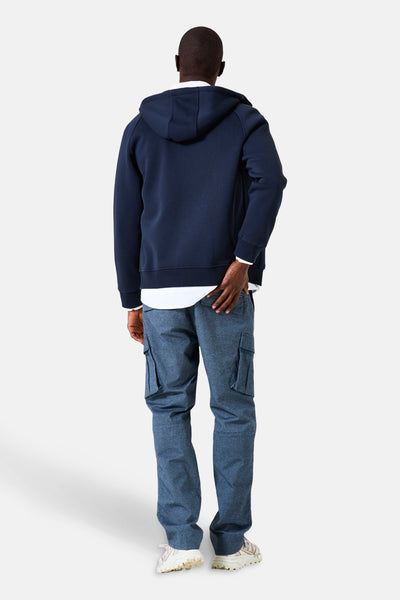 Blauwe GARCIA-gilet, gedragen over een wit overhemd en een blauwe spijkerbroek met cargozakken, achtergezicht.