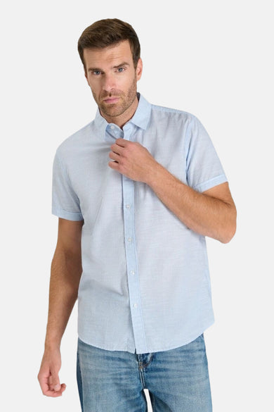Chemise à manches courtes bleue de Le Temps des Cerises, portée avec un jean, sur fond uni.
