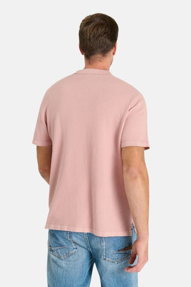 Polo rose en maille gaufrée de Le Temps des Cerises, porté avec un jean délavé, vue de dos.