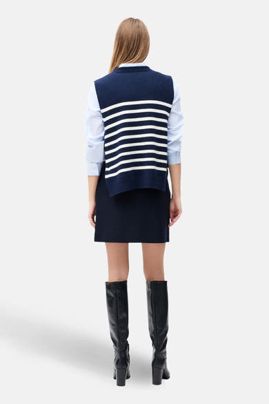Débardeur bleu à rayures blanches de Caroll, porté sur une chemise bleue avec une jupe bleu marine et des bottes noires.
