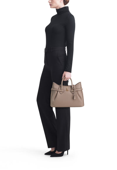 Taupe leather handbag by Céline with gold-tone hardware, structured silhouette, top handles, and front tassel detail, shown in side view on model wearing black outfit.