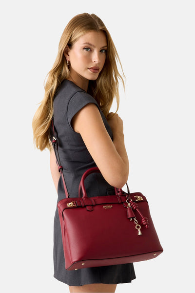 Rode handtas van imitatieleer van Guess, met een decoratieve sleutelbedel, gedragen over de schouder met een grijze jurk.