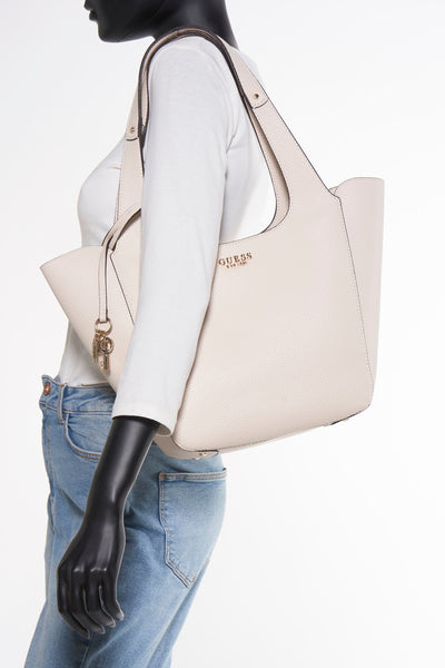 Sac à bandoulière écru de Guess, avec bretelles sur une mannequin portant un t-shirt blanc et un jean.
