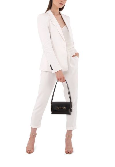 Sac à bandoulière noir de Guess avec bandoulière fine porté par un mannequin en tailleur pantalon blanc.
