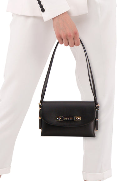 Sac à bandoulière noir de Guess, porté à la main, avec détails dorés et tenue blanche.
