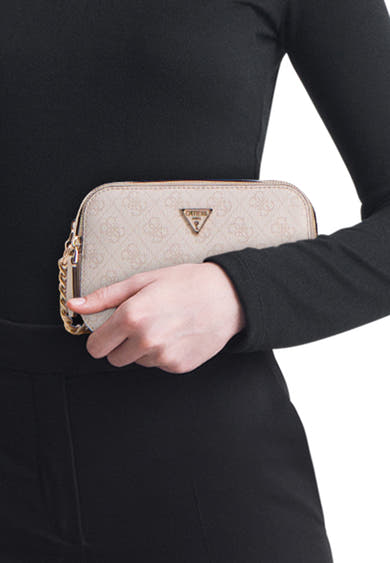 Sac à bandoulière beige de Guess, avec motif logo et détails dorés, porté avec un chemisier et un pantalon noirs.

