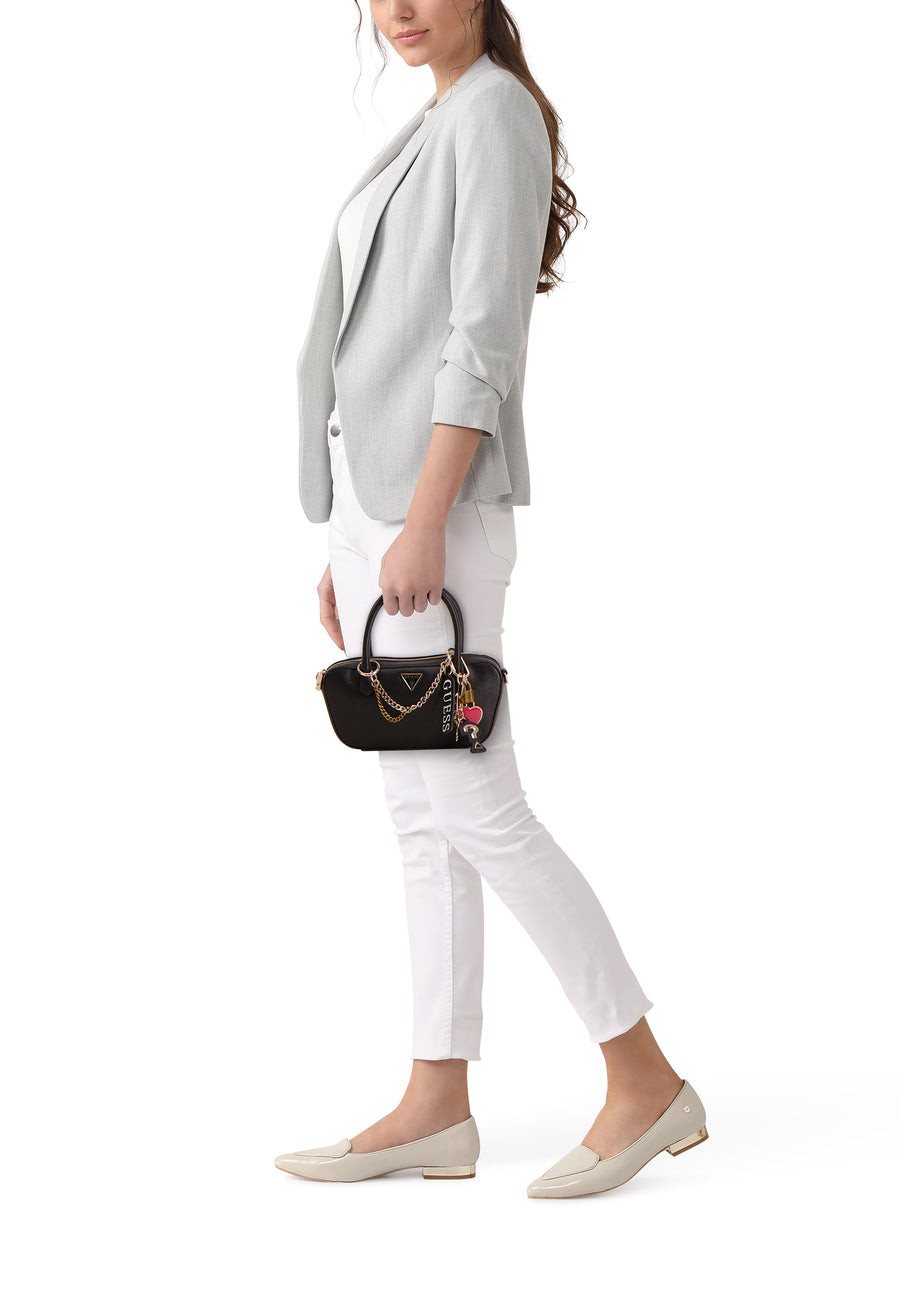 Sac à main noir de Guess avec chaîne décorative et breloques, porté avec un blazer gris et un pantalon blanc.
