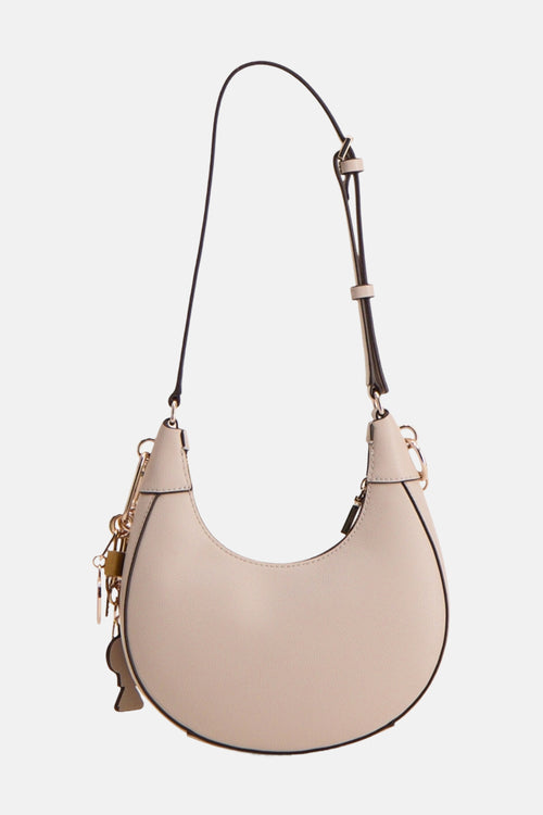 Sac à bandoulière beige de Guess®, avec une bandoulière noire réglable et des breloques dorées décoratives.
