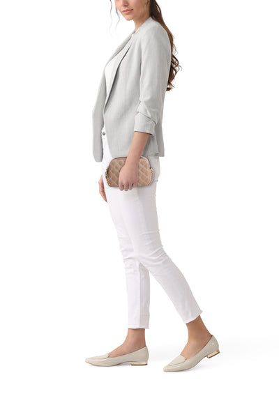 Sac à bandoulière beige de Guess®, porté avec un blazer gris, un pantalon blanc et des chaussures plates.
