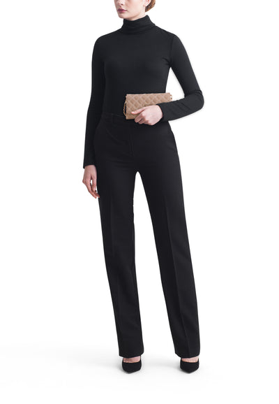 Sac à bandoulière beige de Guess, porté avec un pantalon noir taille haute et un pull noir à col roulé.