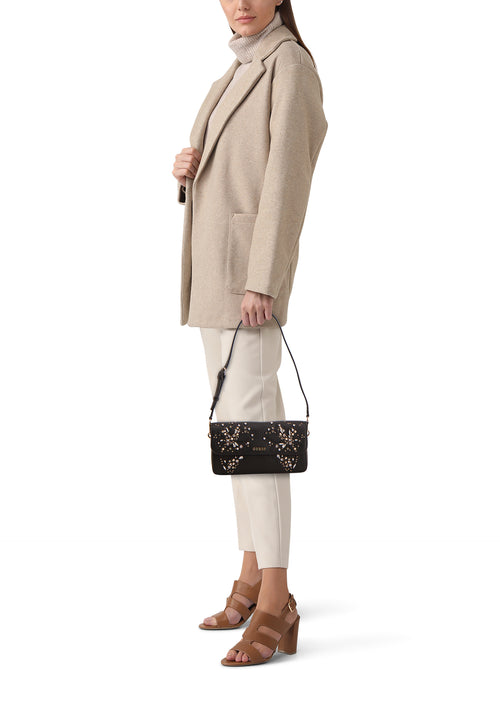 Zwarte Guess schoudertas versierd met decoratieve vlinders, gedragen met een beige jas en bruine hakken.
