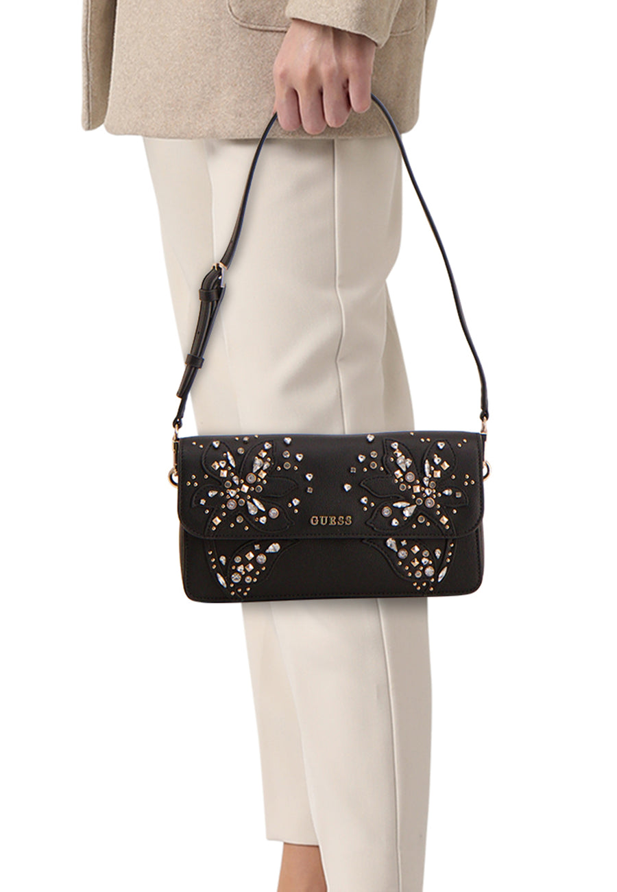 Zwarte Guess schoudertas versierd met glinsterende bloemenpatronen, gedragen met een beige jas en een witte broek.