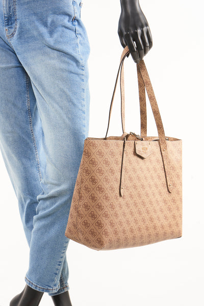 Sac à bandoulière brun de Guess avec un motif monogramme et porté avec un jean bleu.