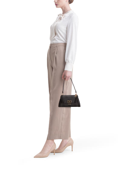 Zwarte Guess schoudertas met logoprint, gedragen met een witte blouse en een beige broek.