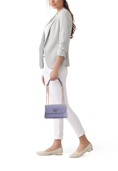 Blauwe Guess schoudertas met print, gedragen door een model met een grijze blazer en een witte broek.
