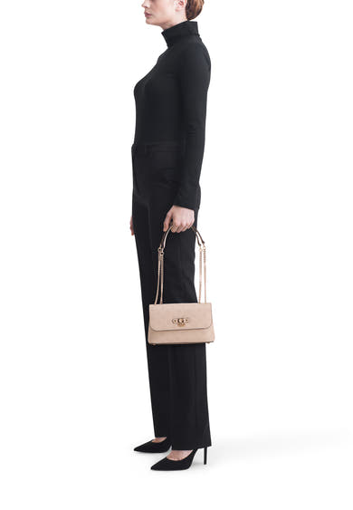 Beige Guess schoudertas, in de hand gedragen met een decoratieve ketting, gedragen met een zwarte trui en broek.