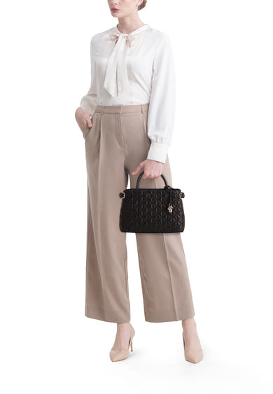 Zwarte Guess handtas, met ruitvormig gewatteerd patroon en gouden afwerkingen, gedragen met een beige blouse en broek.