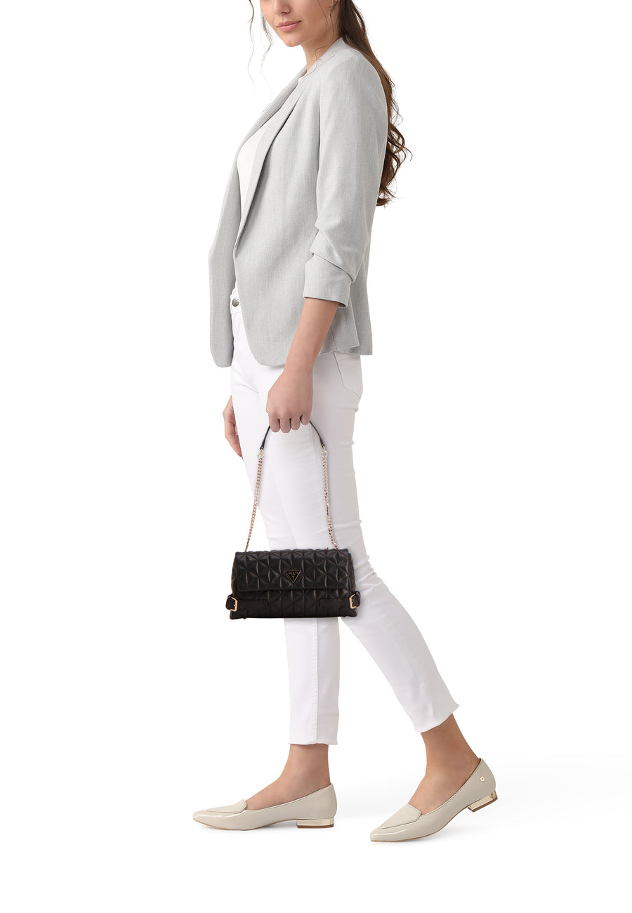 Zwarte Guess schoudertas, gedragen door een vrouw in een grijze blazer en een witte broek.