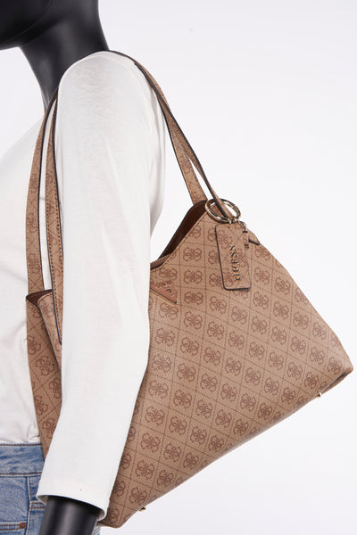 Sac à main marron Guess, avec motif imprimé et détails dorés, porté sur un mannequin en chemise blanche et jeans.

