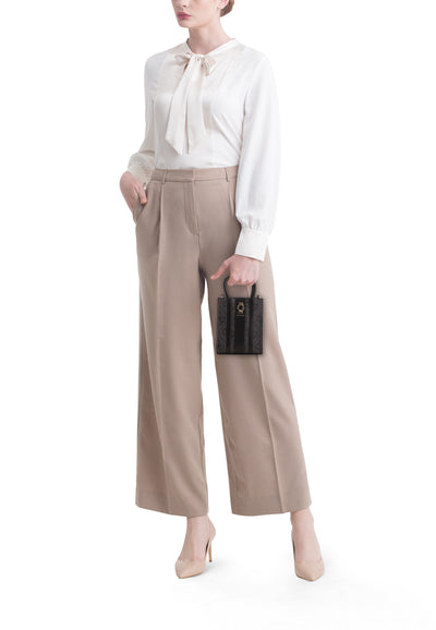 Sac à bandoulière noir de Guess, porté avec un chemisier blanc et un pantalon beige.