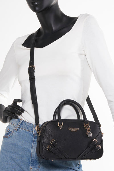 Sac à main noir de Guess, avec bandoulière et détails dorés, porté avec un jean bleu et un T-shirt blanc.
